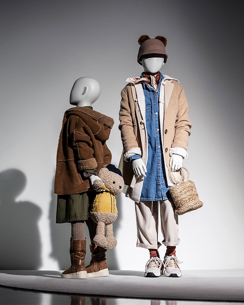 two girl kids mannequins from the kids collections standing together with one holding a bear backpack
